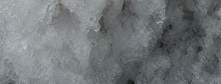 Neve granulada vista bem de perto, com grãos grossos e aspecto de gelo sujo.