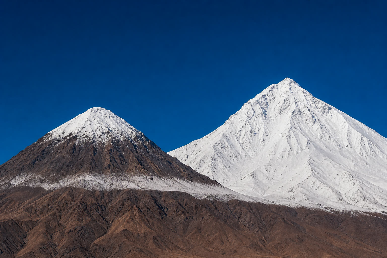 Dois picos dos Andes lado a lado: o mais alto todo branco, o mais baixo com rocha exposta abaixo de uma linha de neve.