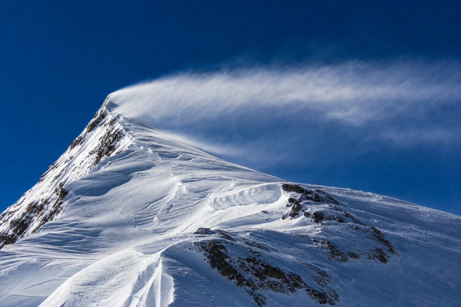 Vento forte arrastando um penacho de neve solta do alto de uma crista dos Andes.